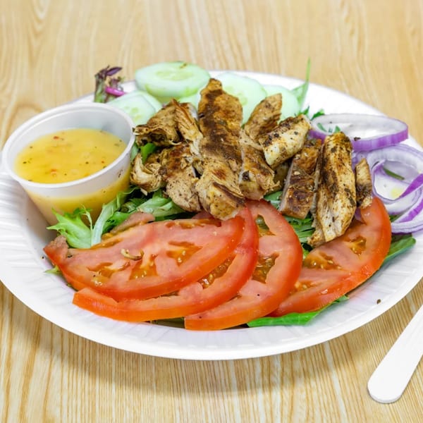 Grilled chicken salad with lettuce, tomatoes, cucumbers, red onions, and a side of dressing.
