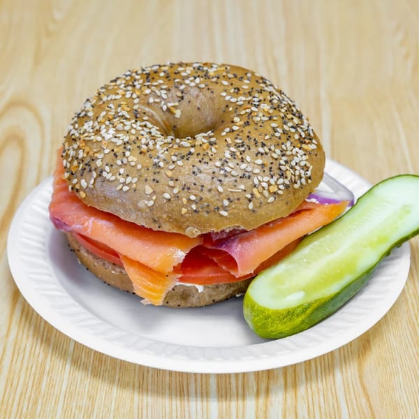 Everything bagel with lox, cream cheese, tomato, onion, and a pickle spear on a white plate.