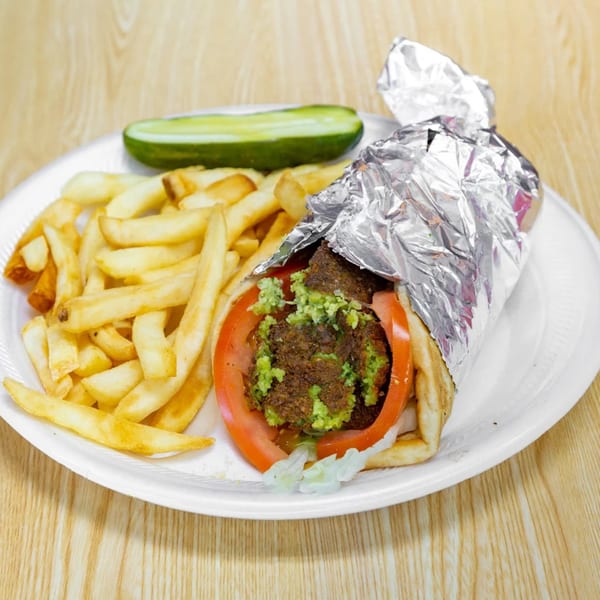 Falafel wrap with tomatoes, lettuce, and green sauce, served with fries and a pickle.