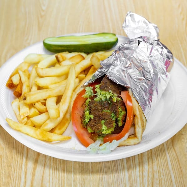 Falafel sandwich with tomatoes, lettuce, and guacamole, served with fries and a pickle.