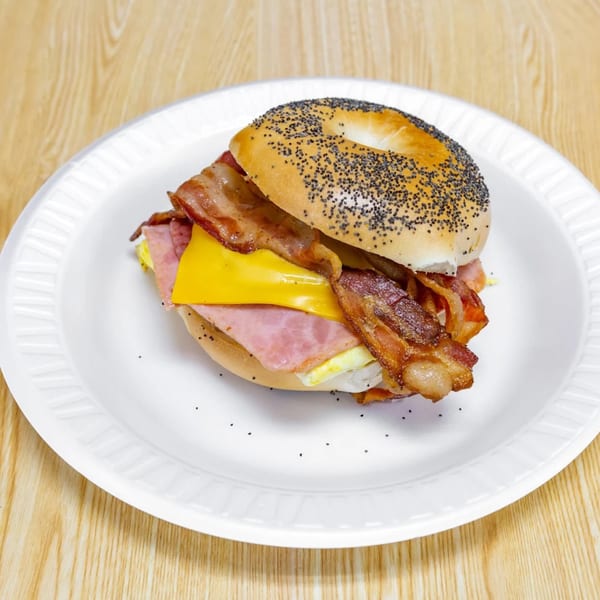 Poppy seed bagel sandwich with bacon, ham, cheese, and egg on a white plate.