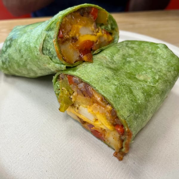 Two halves of a green tortilla wrap filled with eggs, cheese, potatoes, and peppers on a white plate.